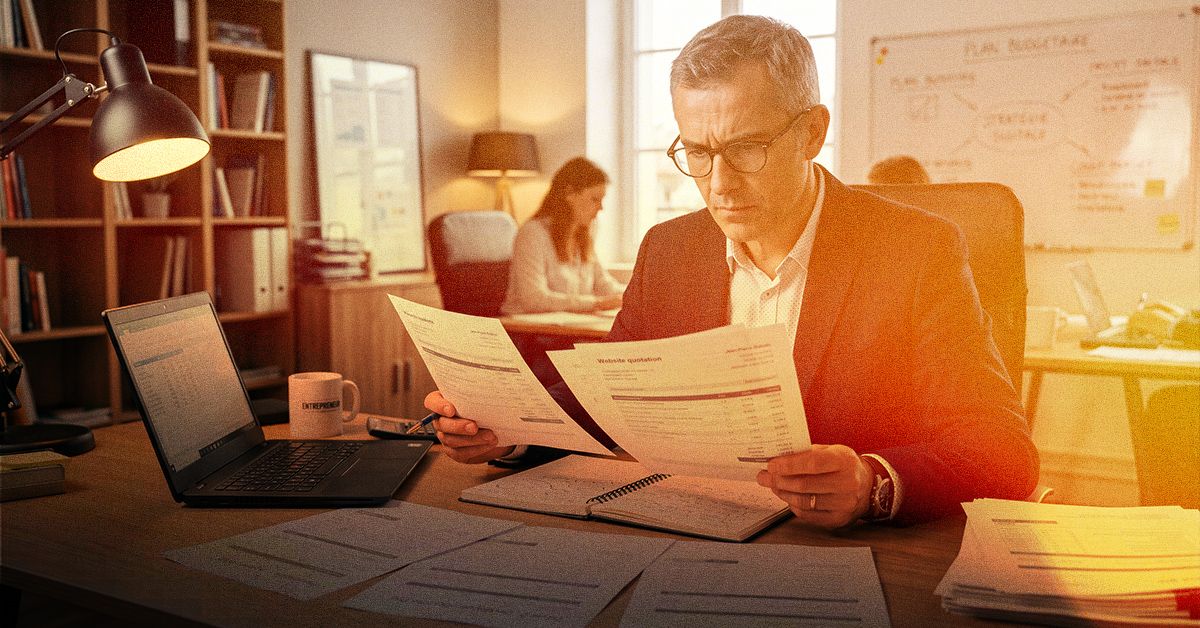 Dirigeant d'entreprise comparant deux devis de création de site internet à son bureau, un ordinateur portable et un carnet ouvert devant lui